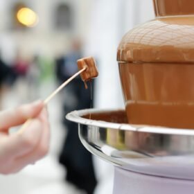 Woman holding marshmallow and frosting its in chocolate fondue fountain.